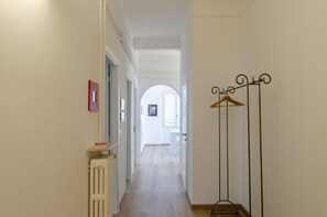 A narrow hallway with white walls, a radiator, and a coat rack.
