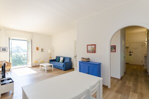 A spacious living room with a blue sofa, a white coffee table, and a dining area with a white table.