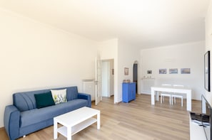 A modern living room with a blue sofa, white coffee table, and a dining area with a white table and chairs.