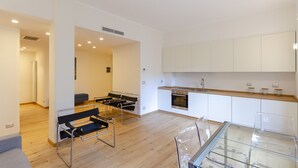 A modern kitchen with white cabinets, a stainless steel oven, and a glass dining table. - JOIVY 3-Bedroom Family Apartment in Santa Margherita near Beach (Santa Margherita Ligure)