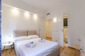 Een hotelkamer met een groot bed, een nachtkastje met een lamp, en een badkamer zichtbaar door een open deur.
