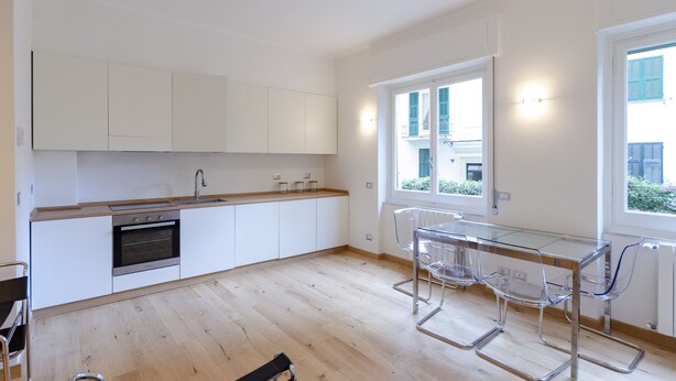 A modern kitchen with white cabinets, a stainless steel oven, and a glass dining table with chairs. - JOIVY 3-Bedroom Family Apartment in Santa Margherita near Beach (Santa Margherita Ligure)