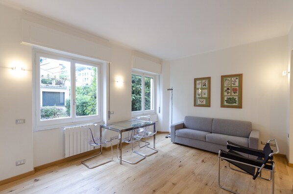 Een moderne woonkamer met een glazen eettafel, een grijze bank en een zwarte stoel.