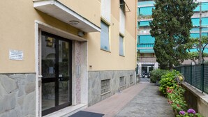 A building entrance with a stone facade, a black door, and a small garden with flowers. - JOIVY 3-Bedroom Family Apartment in Santa Margherita near Beach (Santa Margherita Ligure)