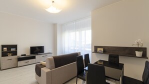 A modern living room with a sofa, TV, dining table, chairs, and a plant. - JOIVY Lovely Apt On The Historical Street Via Cantore (Genoa)