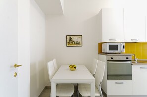 A small, clean kitchen with white cabinets, a microwave, and a stove. There is a dining table with chairs and a small yellow flower vase.