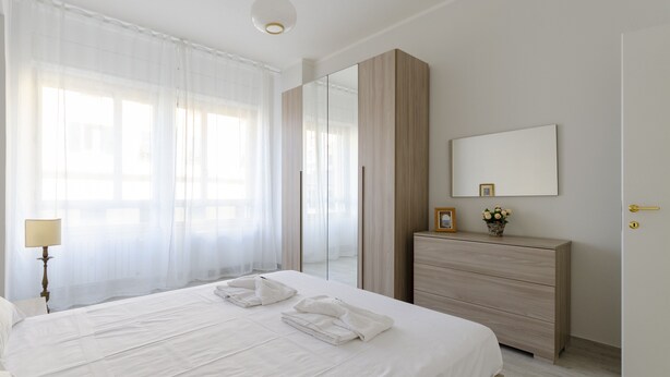 A hotel room with a bed, a dresser, a mirror, and a lamp. - JOIVY Lovely Apt On The Historical Street Via Cantore (Genoa)