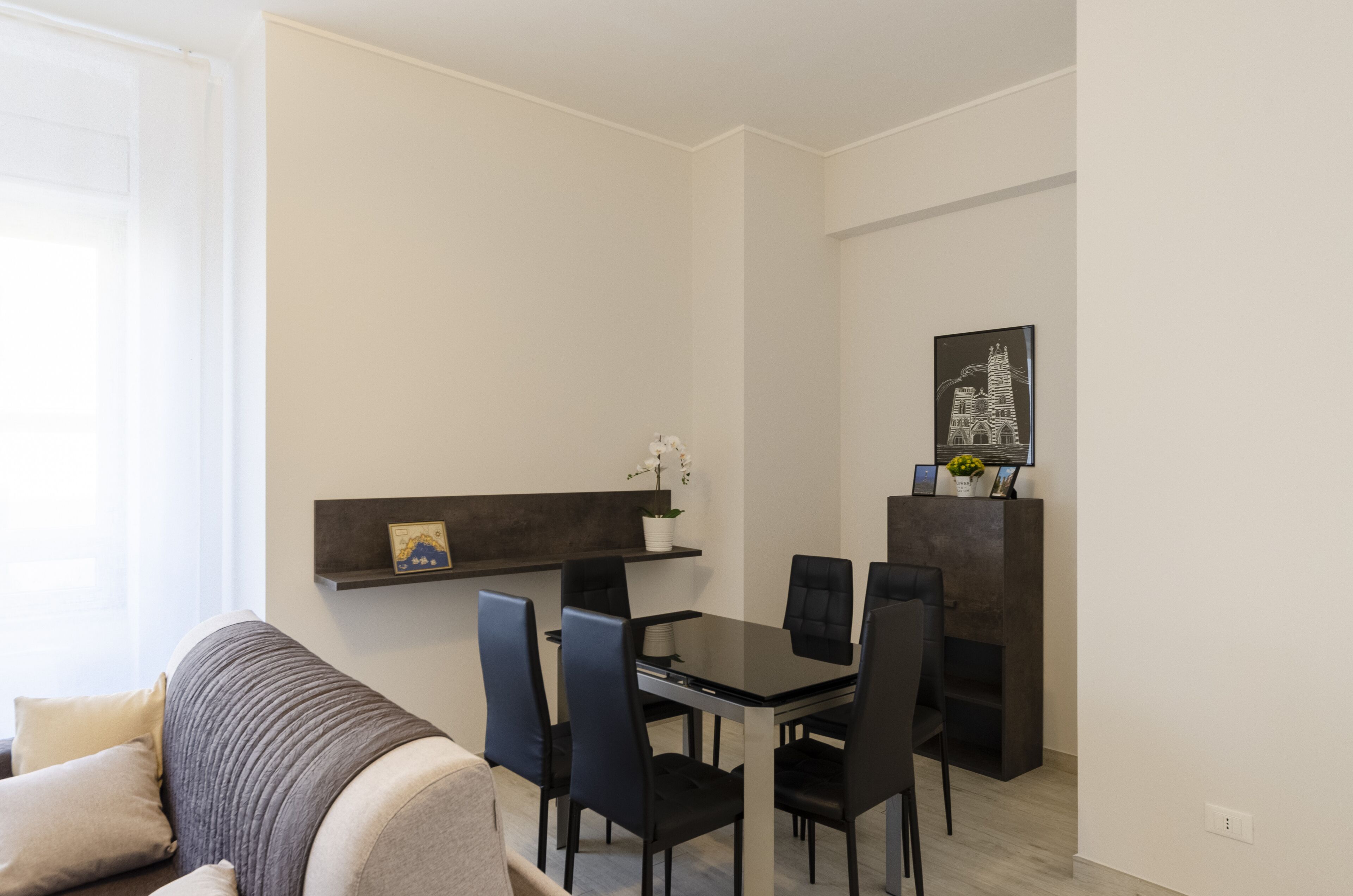 A modern living room with a sofa, a dining table with chairs, a small plant, and a framed picture on the wall.