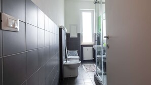 A modern bathroom with dark tiles, a toilet, a bidet, and a glass shower enclosure. - JOIVY Spacious Family Flat For 6 People In Genova (Genoa)