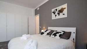 A neatly made bed with rolled towels, a world map on the wall, and a wardrobe with a door. - JOIVY Spacious Family Flat For 6 People In Genova (Genoa)