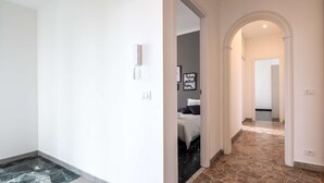 A hallway with a marble floor, a bed with a gray bedspread, and a stone-tiled floor leading to another room. - JOIVY Spacious Family Flat For 6 People In Genova (Genoa)