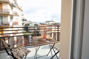 Un balcon avec une table en bois, deux chaises, une bouteille et un bol de collations.