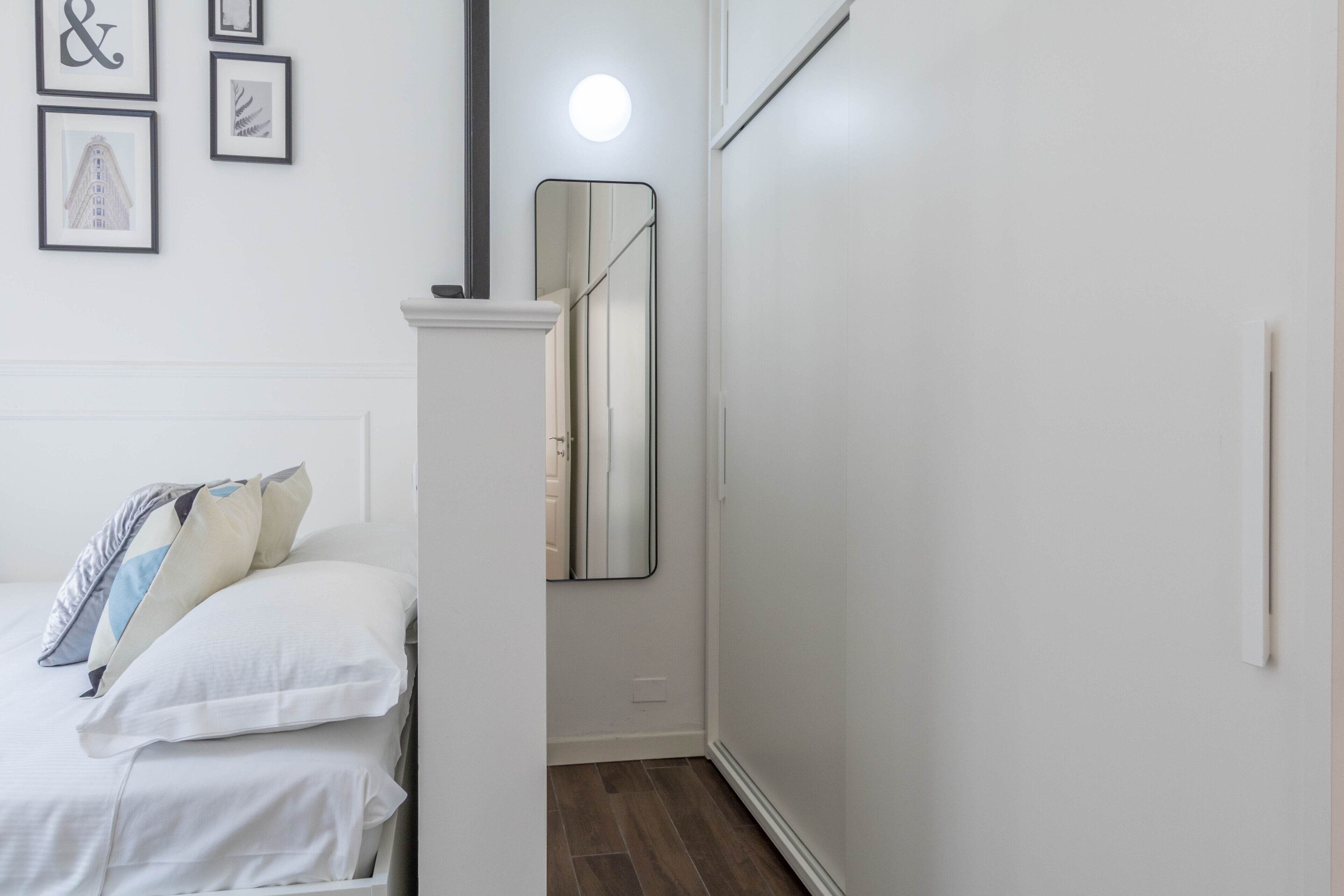 A bedroom with a bed, a wardrobe, a mirror, and framed pictures on the wall.