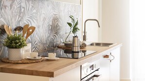 A kitchen with a wooden countertop, a sink, and a backsplash with a leaf pattern. There are utensils, a plant, and a kettle on the counter. - JOIVY Charming Flat Next to Duomo di Como (Como)