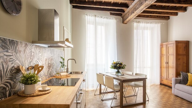 A modern kitchen with a wooden countertop, a built-in stove, and a dining area with a table and chairs. - JOIVY Charming Flat Next to Duomo di Como (Como)