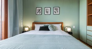 A neatly made bed with a wooden headboard, two bedside lamps, and three framed artworks on the wall.