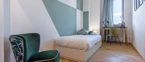 A bedroom with a bed, a desk, a chair, and a window with curtains.