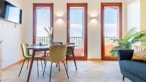 Ein Essbereich mit Tisch und Stühlen, einem an der Wand befestigten Fernseher und einem Balkon mit Aussicht.