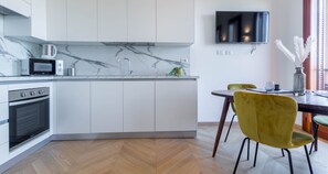 A modern kitchen with white cabinets, a microwave, a kettle, and a dining area with a table and chairs.