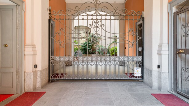 A gated entrance with a metal gate, a red carpet, and a view of a building with columns and a door. - JOIVY Bright And Cozy Studio For 2 In Porta Genova (Milan)
