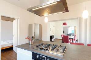 A modern kitchen with a gas stove, a refrigerator, and a dining area with red chairs.