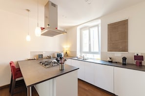 Eine moderne Küche mit einer Kochinsel, weißen Schränken, einem eingebauten Herd und einem Fenster mit Jalousien.