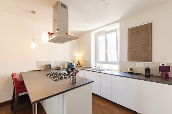 A modern kitchen with a central island, white cabinetry, a built-in stove, and a window with blinds.