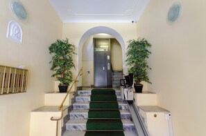 A hotel lobby with marble stairs, a reception desk, and potted plants.