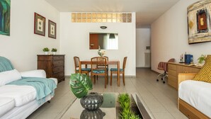 Ein modernes Wohnzimmer mit einem weißen Sofa, einem Esstisch mit Stühlen, einem Couchtisch und einer großen Pflanze.