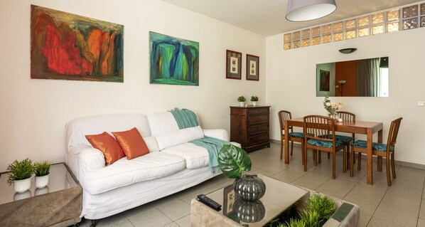 A living room with a white sofa, a dining table with chairs, and artwork on the walls.