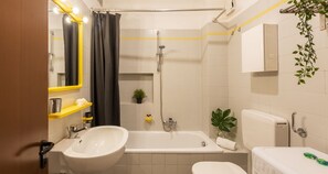 A bathroom with a bathtub, a sink, and a toilet. There are yellow shelves, a mirror, and a plant.