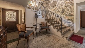 Eine Steintreppe führt zu einer zweiten Etage, Holzstühle, ein kleiner Tisch und eine Tür mit dekorativer Glasscheibe.