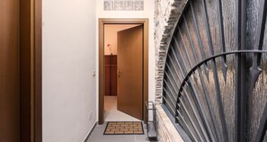A narrow hallway with a wooden door at the end, a metal gate, and a small doormat on the floor.