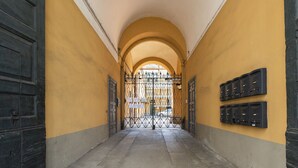 Ein Korridor mit gelben Wänden, schwarzen Türen und einem Metallgitter am Ende.