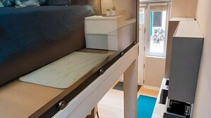 Une petite pièce comprenant un lit superposé, un bureau, une chaise et un coin cuisine.