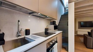 Une cuisine moderne dotée d’un évier en acier inoxydable, d’un four encastré et d’un four à micro-ondes. Un escalier mène à un espace de vie équipé d’un téléviseur à écran plat.