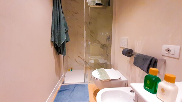 Un baño con cabina de ducha de vidrio, inodoro, lavamanos y artículos de aseo en la encimera.