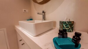 A bathroom with a white sink, a mirror, a towel dispenser, and a box of tissues on the counter.