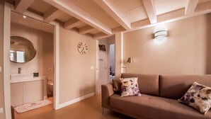A living room with a beige sofa, a round mirror, a wall clock, and a small table with a lamp.