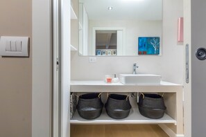 A modern bathroom with a white vanity, a mirror, and three woven baskets on a shelf. - JOIVY Gorgeous Loft For 4 Near Arco Della Pace (Milan)
