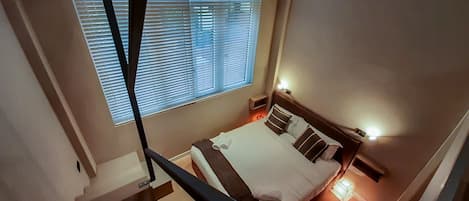 Un dormitorio con una cama, una ventana con persianas, una mesita de noche con lámpara y un estante pequeño.
