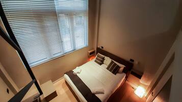 Una camera da letto con un letto, cuscini, un comodino e una finestra con persiane.