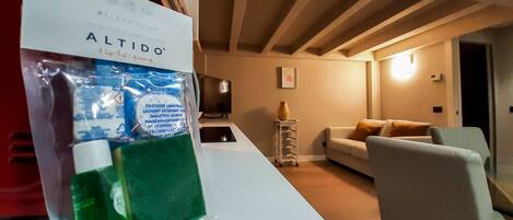A living room with a sofa, a TV, and a small table with a vase. There is a bag of cleaning supplies on the table.