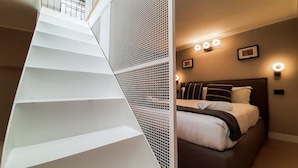 Quarto de hotel moderno com escada, cama com cabeceira e iluminação embutida na parede.