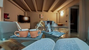 Uma sala de estar acolhedora com uma mesa de centro de vidro, duas canecas cor-de-rosa, um livro, uma cafeteira e uma televisão ao fundo.