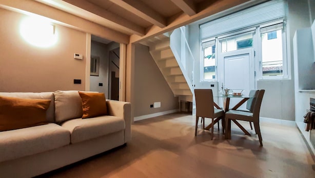 Uma sala de estar moderna com um sofá, uma mesa de jantar com cadeiras e uma escada que leva a um andar superior.