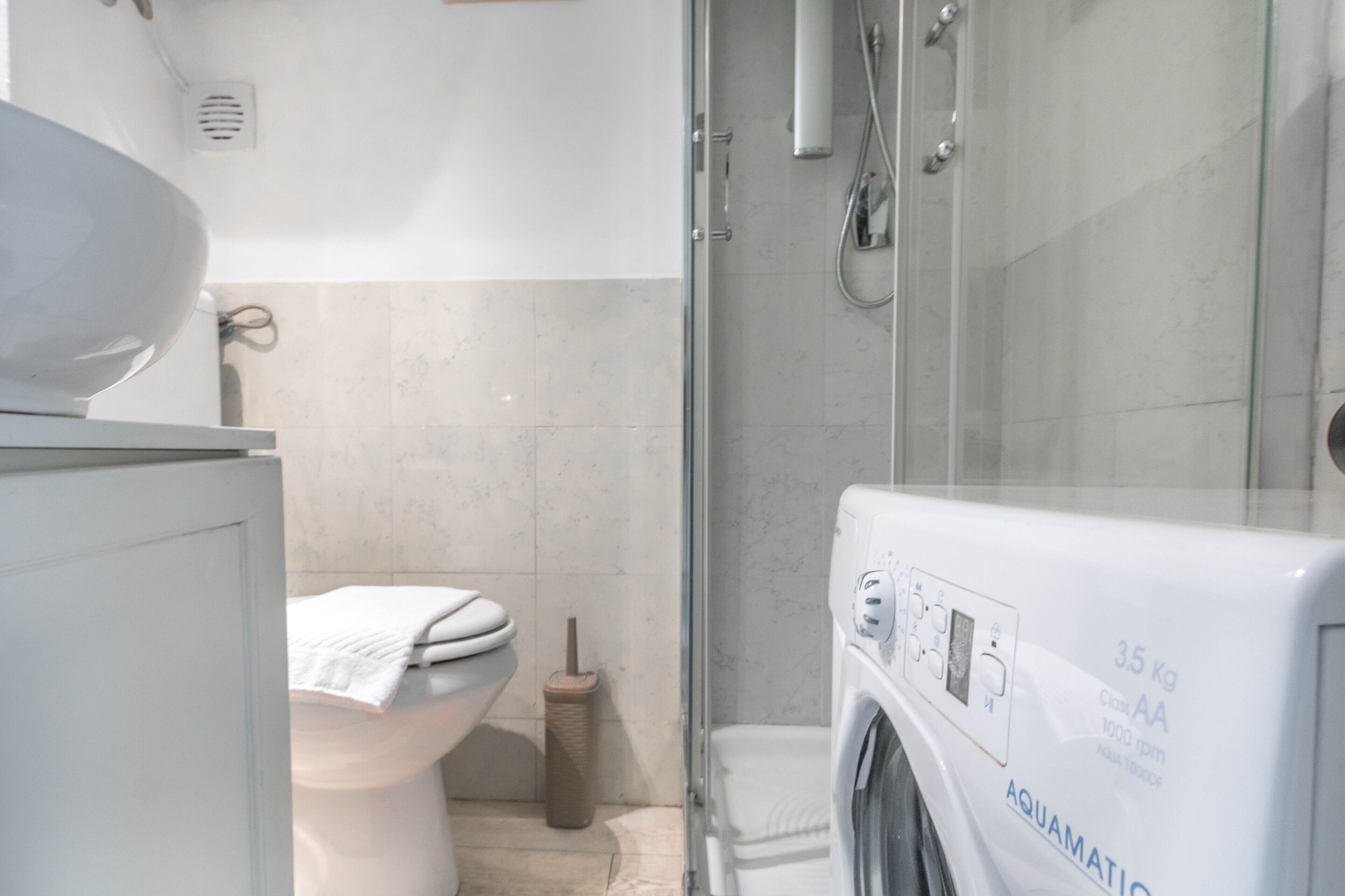 A bathroom with a toilet, a washing machine, and a shower area.