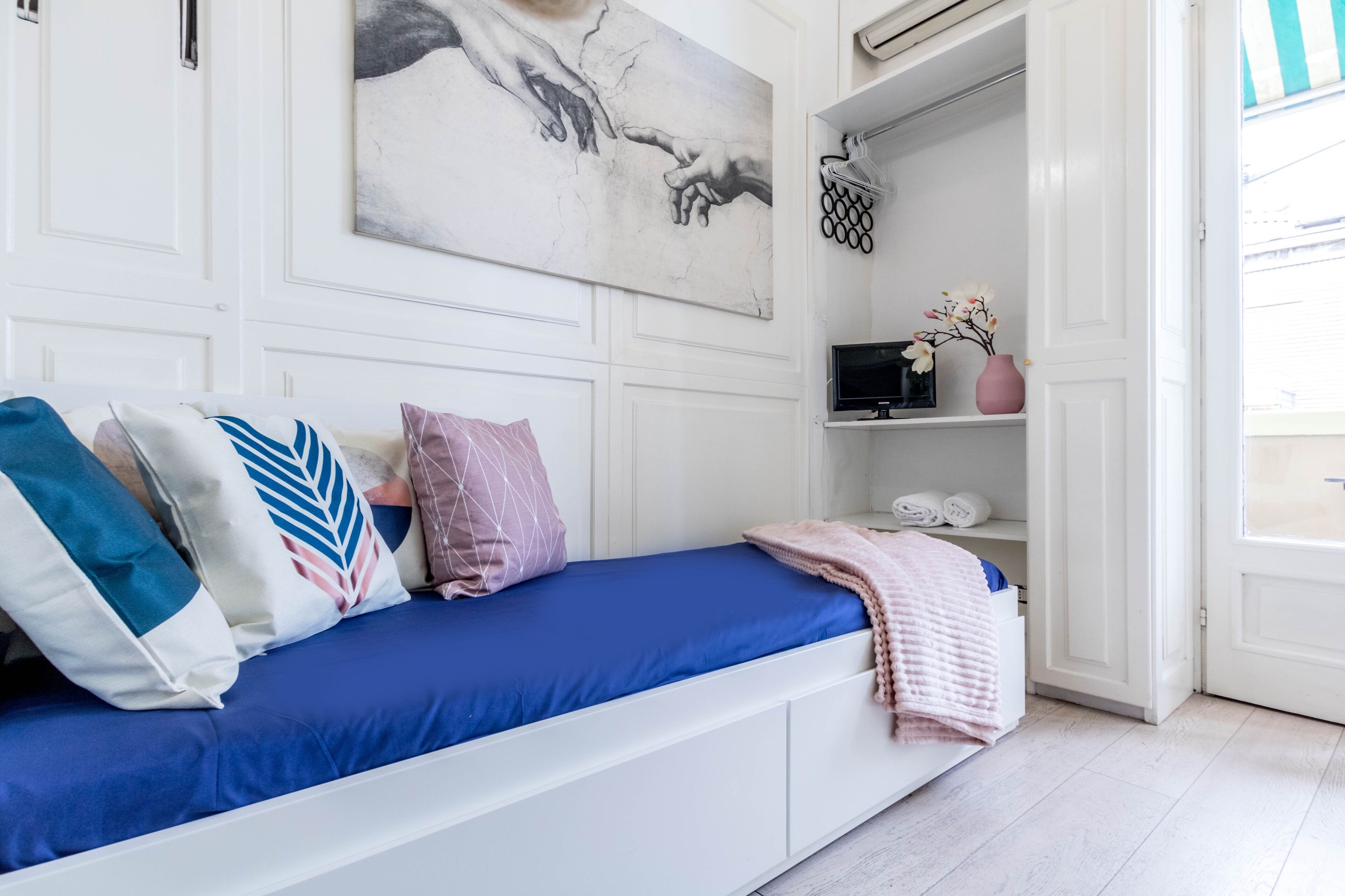 A bedroom with a bed, pillows, a painting, a TV, and a shelf with items.