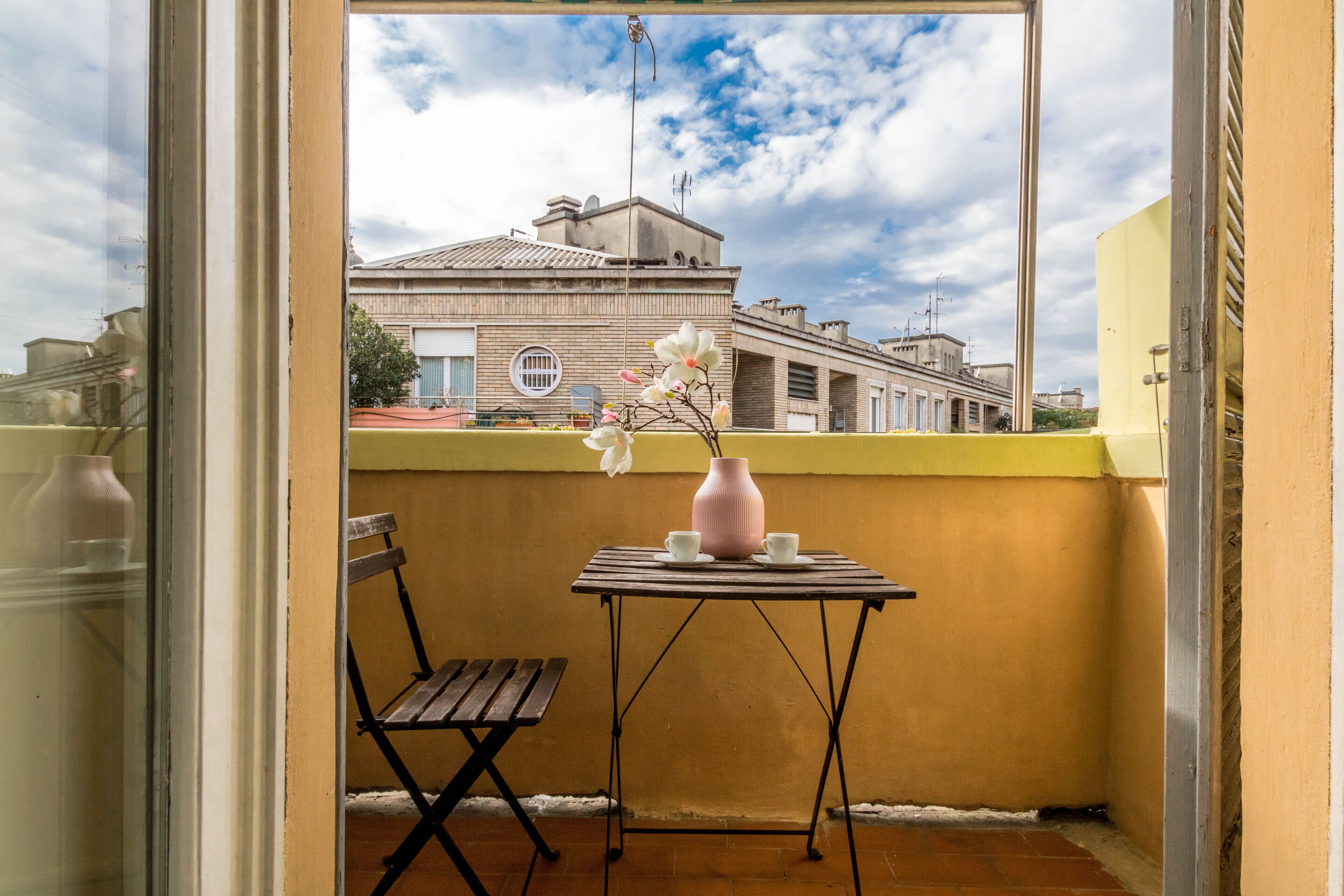 Ein Balkon mit Tisch, Stuhl und einer Blumenvase.