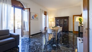 A room with a dining table, chairs, a sofa, and a large window with curtains. - JOIVY Apt For 7 Perfect For Families Close To Beaches (Genoa)